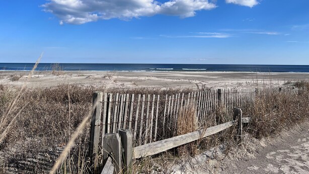 Une plage bordée d’une clôture en bois et où la végétation est sèche.