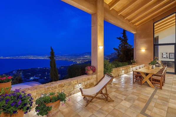 A terrace with a view of the sea at dusk, a wooden table and chairs, and potted plants. - Villa Vollard Panoramic Seaview Private Pool (Malevizi)