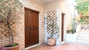 Un muro de ladrillo, una puerta de madera, una planta en maceta, un celosía de madera y una escalera.