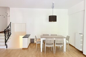 A dining area with a table and chairs, a hanging light fixture, a staircase with a railing, and a radiator. - Location: quiet and central area of ​​Sirolo, 150 meters from the square and the path that leads to the beach, reachable on foot.Description: apartment located on the ground floor with garden. Living room with sofa and dining table - separate kitchen (Sirolo)