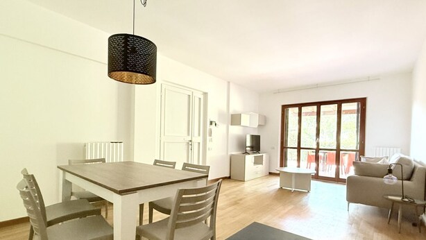 Una sala de estar moderna con una mesa de comedor, sillas, un sofá, un televisor y un ventanal grande.