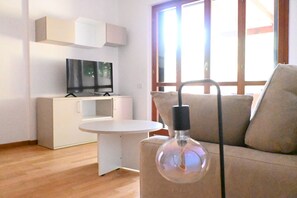 A modern living room with a sofa, a TV on a cabinet, and a round table. - Location: quiet and central area of ​​Sirolo, 150 meters from the square and the path that leads to the beach, reachable on foot.Description: apartment located on the ground floor with garden. Living room with sofa and dining table - separate kitchen (Sirolo)