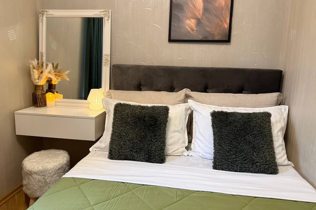 A hotel room with a bed, a nightstand, a mirror, and a wall-mounted picture.