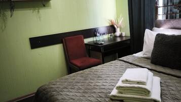 Ett hotellrum med en säng, ett skrivbord, en stol och en hylla med växter.