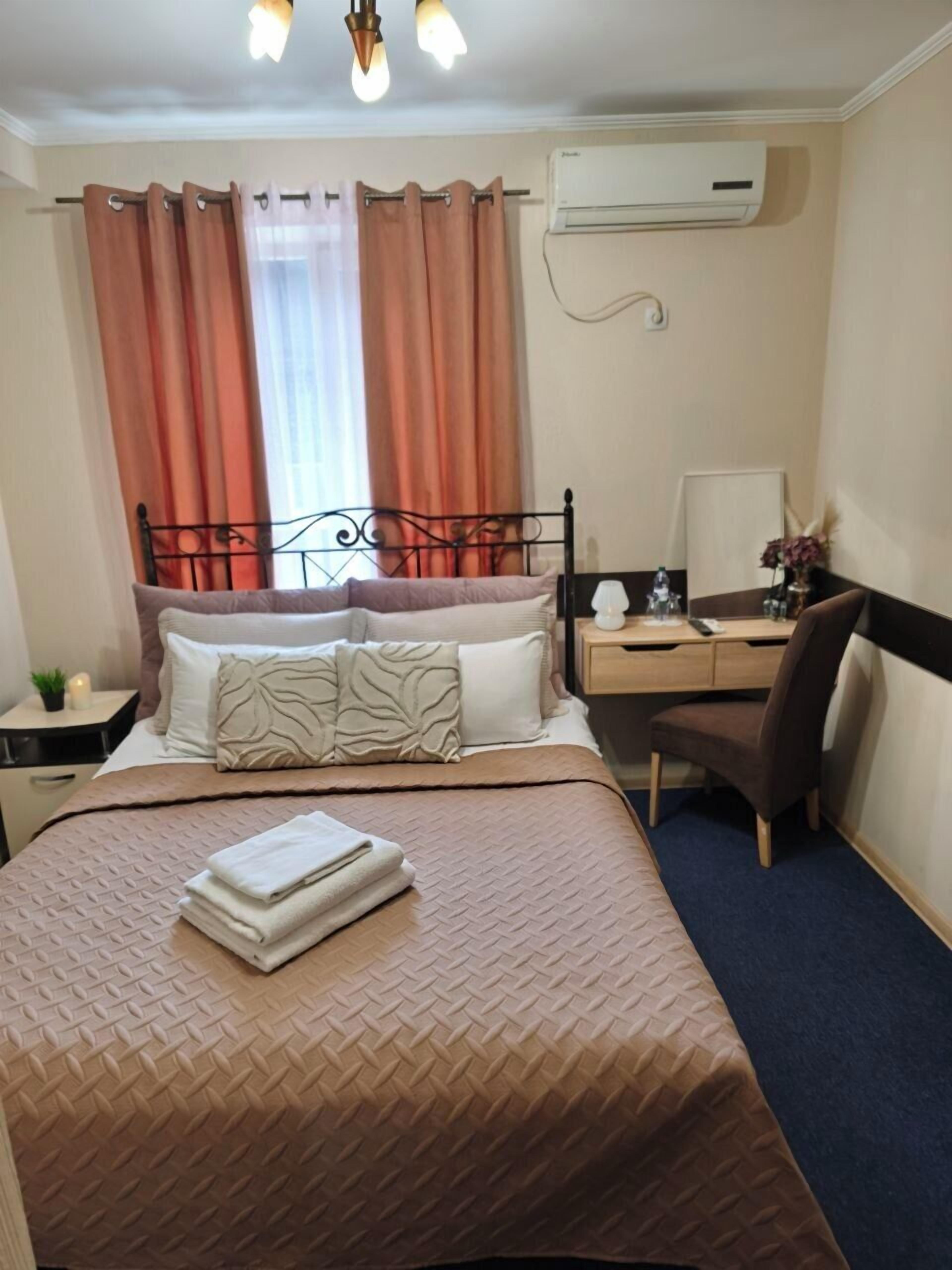 A hotel room with a bed, a desk, a chair, an air conditioner, and a window with curtains.