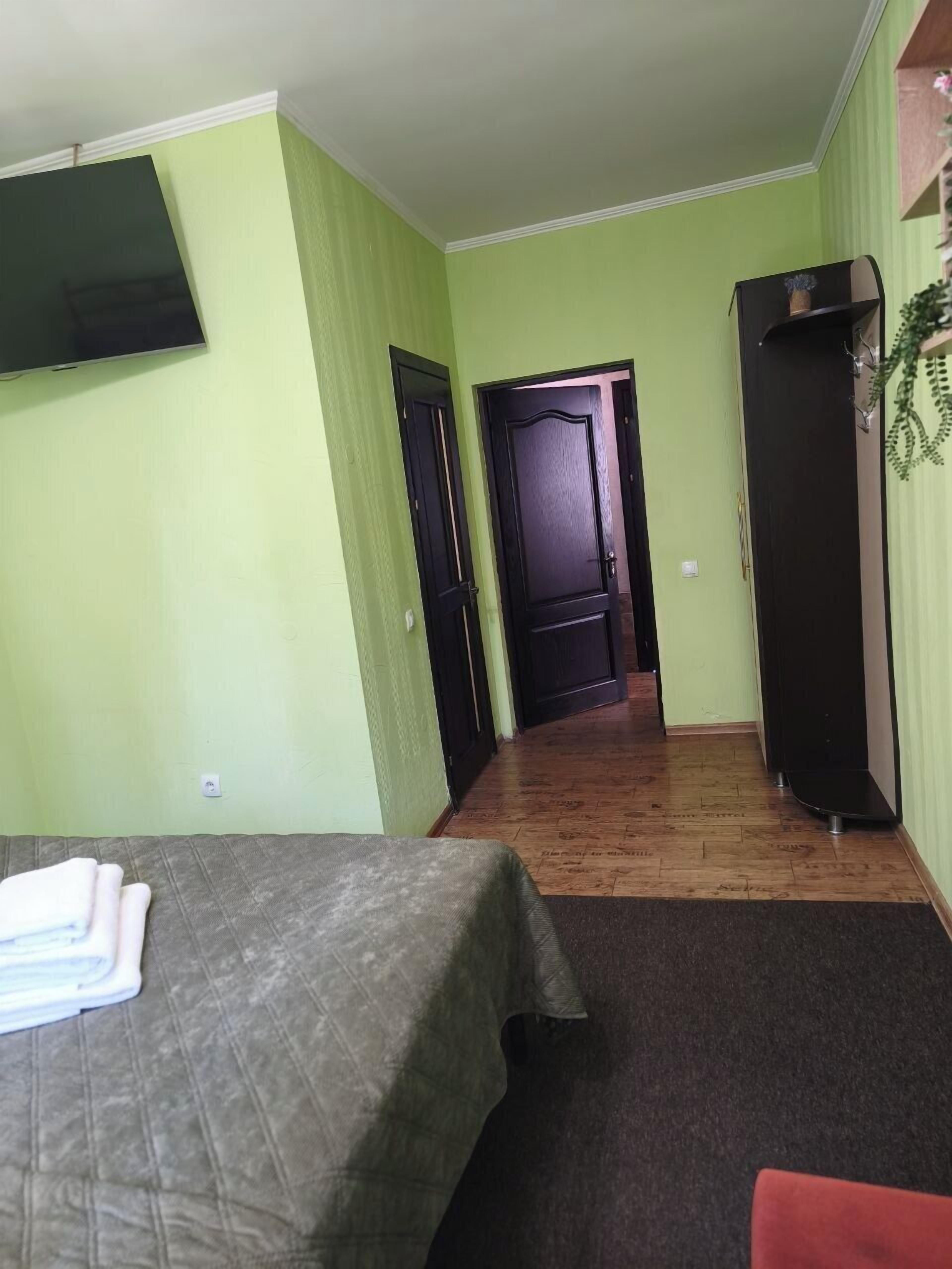 A room with two beds, a TV, a door, a refrigerator, and a hallway leading to another room.
