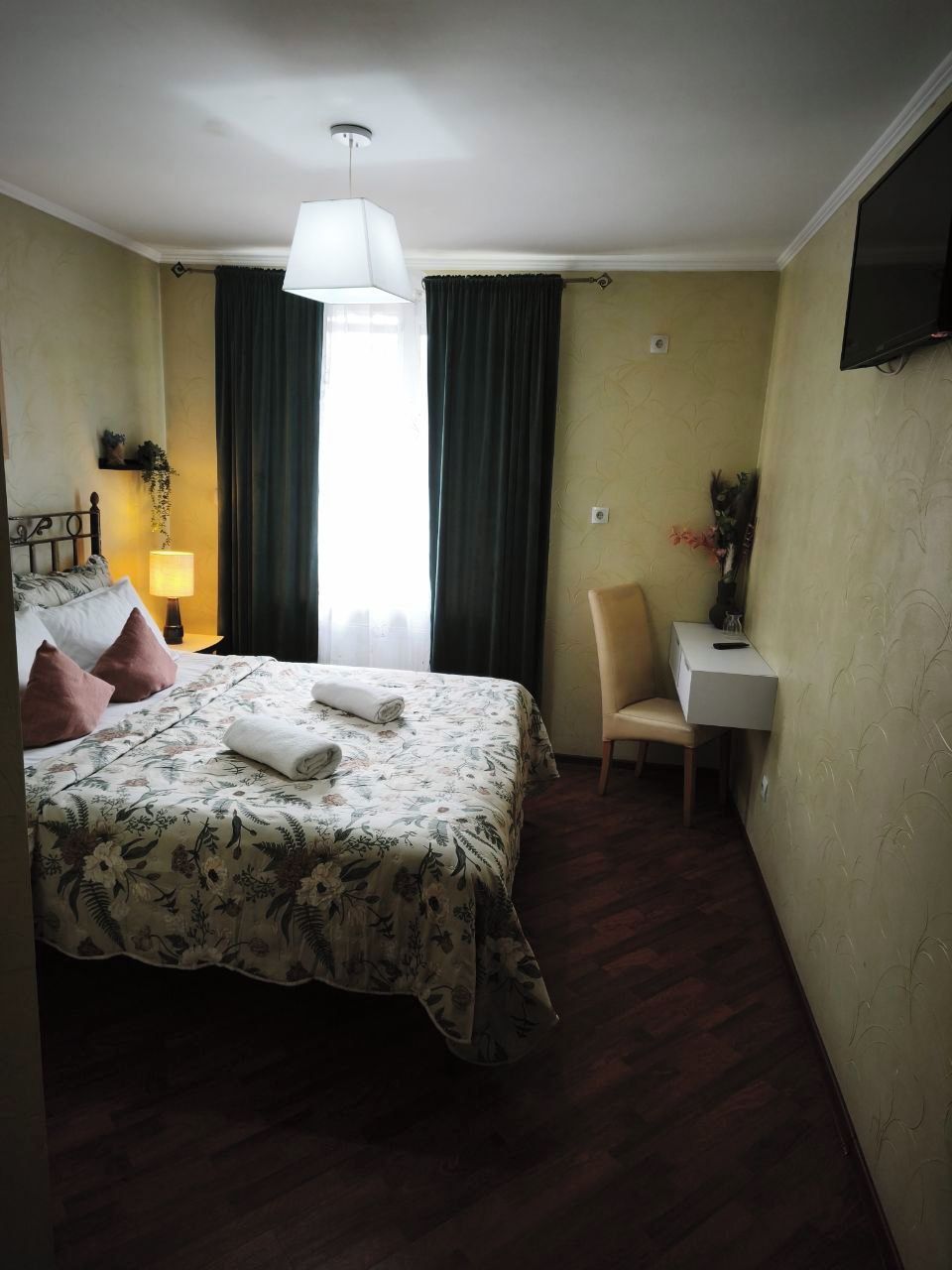 A hotel room with a bed, a desk, a chair, a TV, and a window with curtains.