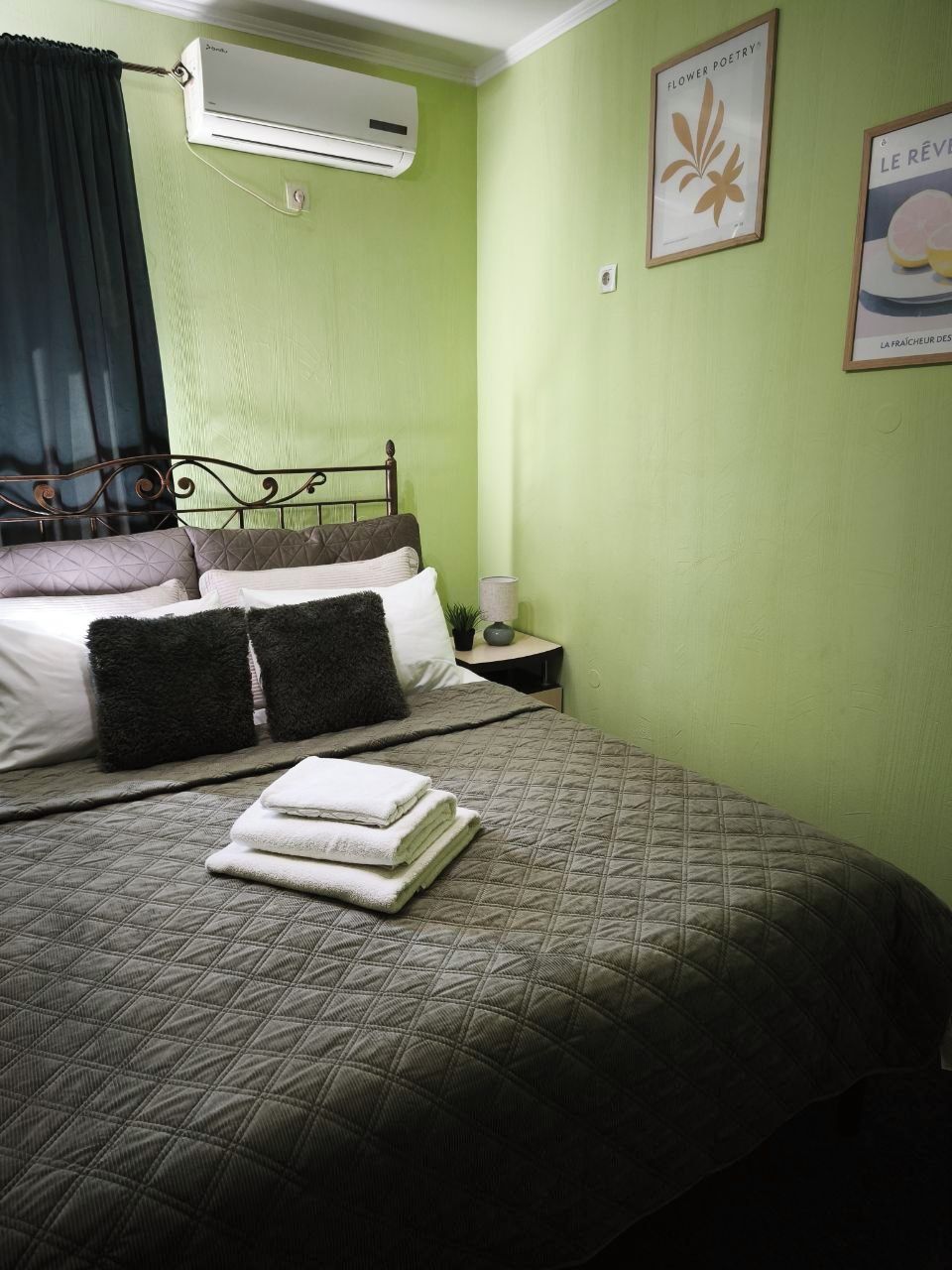 Un dormitorio con cama, almohadas, mesita de noche, aire acondicionado y decoración en la pared.