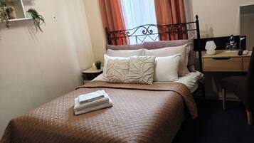 A hotel room with a bed, a desk, a chair, a nightstand, a wall-mounted air conditioner, and a ceiling light fixture.