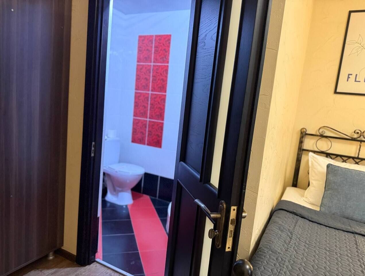 Una habitación de hotel con una cama, una puerta que da a un baño y un suelo rojo y negro.