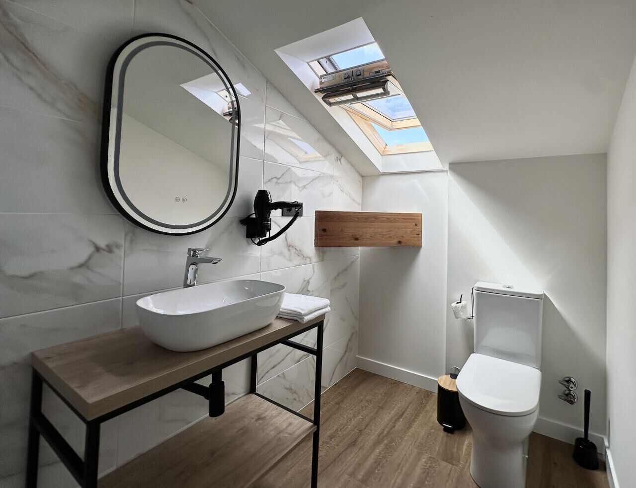 A modern bathroom with a skylight, a large mirror, a vessel sink, and a toilet.