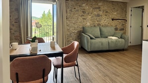 A cozy room with a stone wall, a green sofa, a wooden dining table with chairs, and a window with curtains. - Casa De Postas - Duplex Superior (San Miguel de Meruelo)