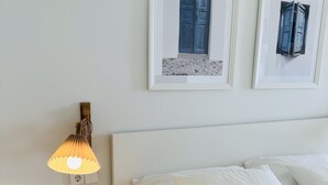 A neatly arranged bedroom with a bed, pillows, a bedside table with a candle, a wall-mounted lamp, and two framed pictures on the wall. - Blue Monis With Amazing Views (Icod de los Vinos)