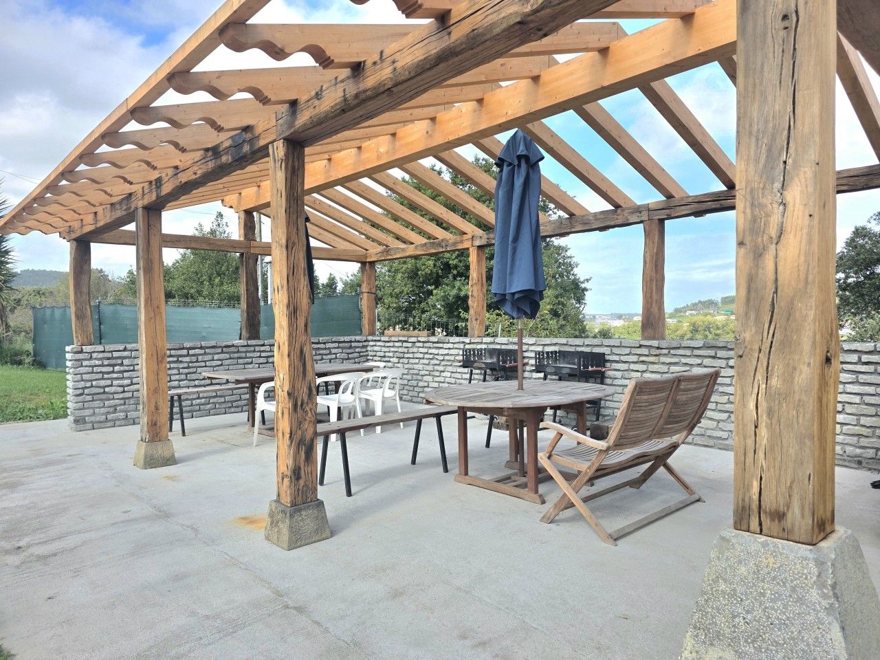 En uteplats med en pergola av trä, stenmurar och utemöbler.