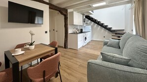 Een modern appartement met een eethoek, een grijze bank, een keuken en een trap.
