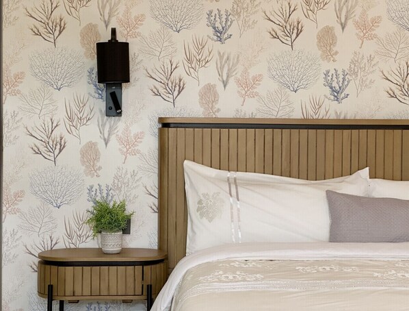 A bedroom with a wooden headboard, a bedside table with a plant, and a wall-mounted light fixture.