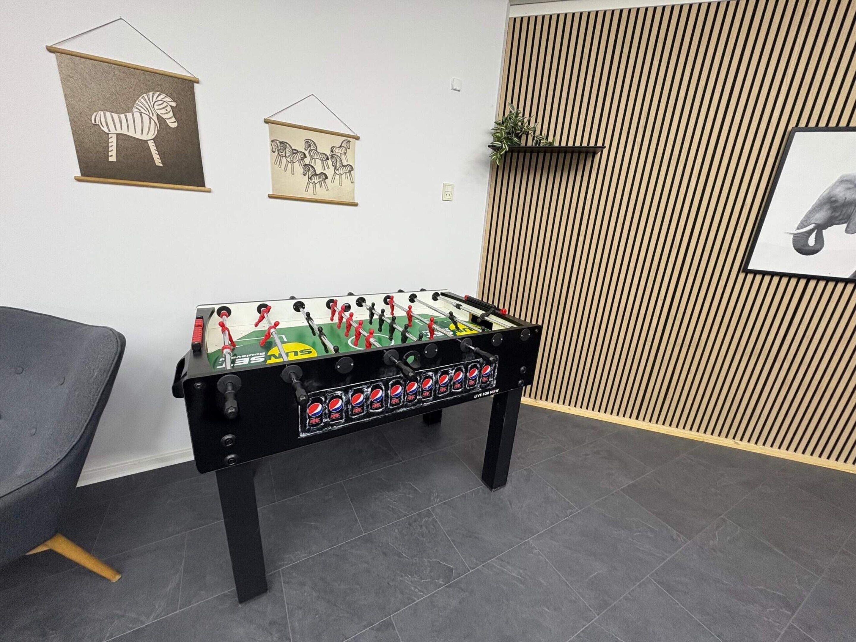 Una habitación con mesa de futbolín, un sillón gris y cuadros en las paredes.