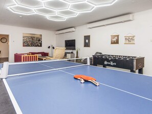 Una stanza con tavolo da ping pong, tavolo da calcio, divano, poltrona e opere d'arte alle pareti.