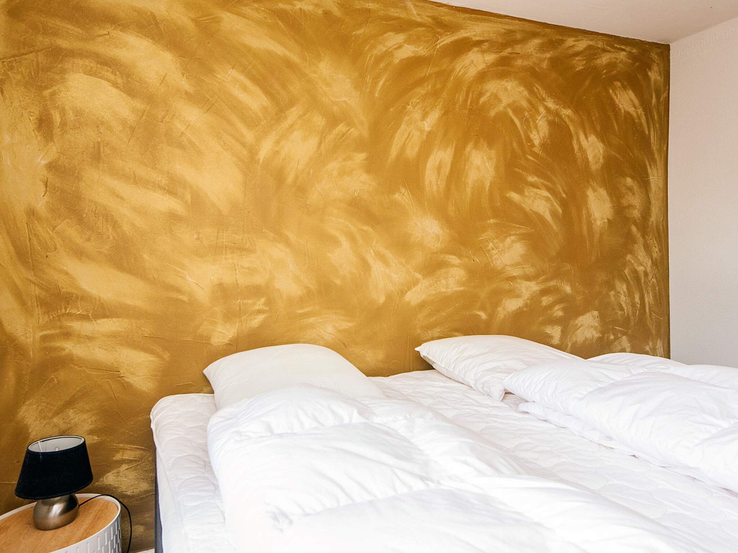 A bed with white bedding in a room with a textured gold wall.