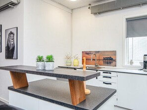 Eine moderne Küche mit Marmorarbeitsplatte, Holzbeinen und Blick auf einen Steg durch ein Fenster.