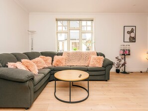 Ein modernes Wohnzimmer mit einem Ecksofa, einem runden Couchtisch, einer Stehlampe und einem großen Fenster.