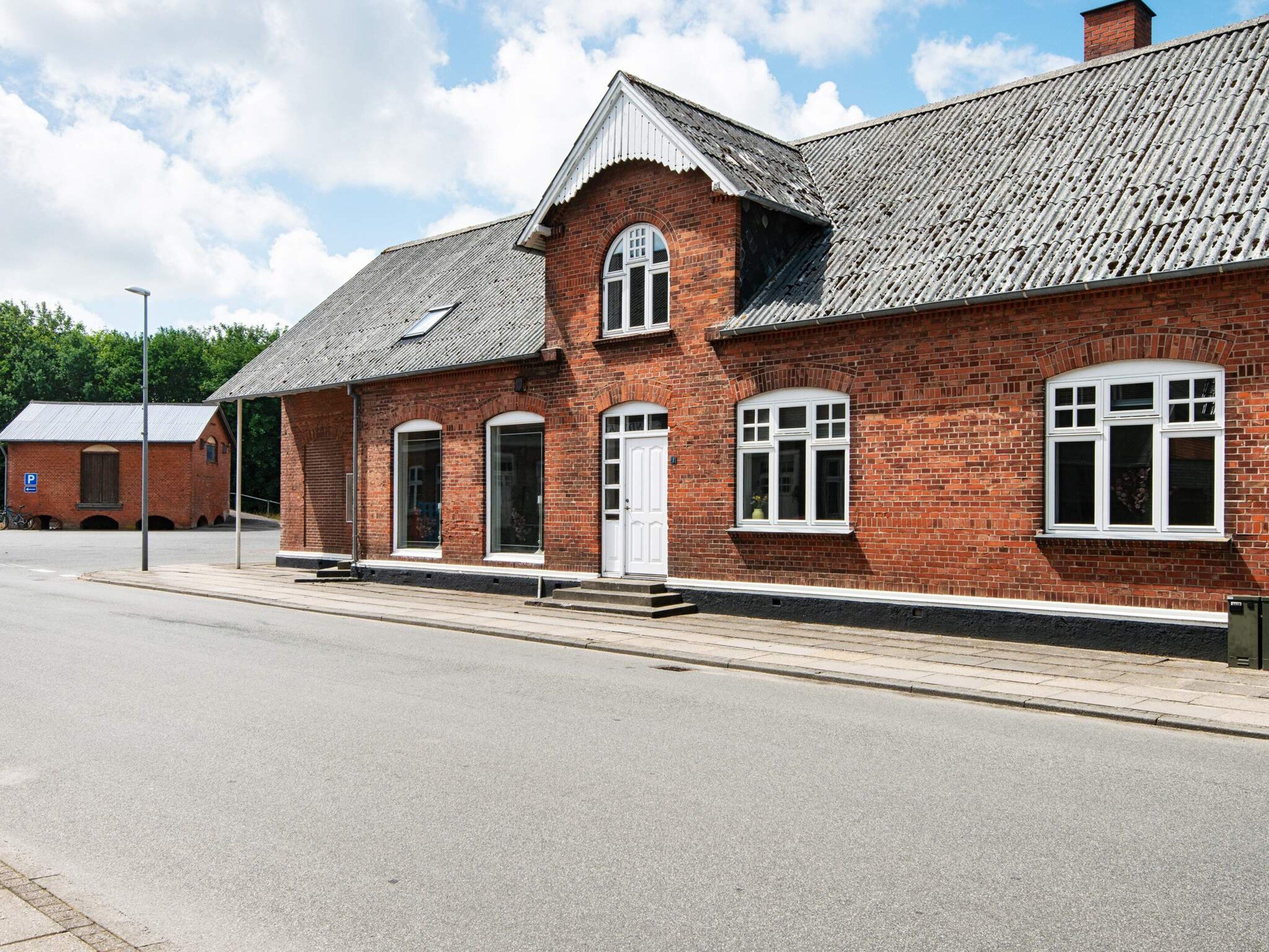 A red brick building with a gabled roof, a white door, and multiple windows.