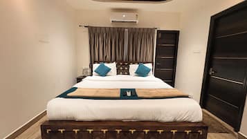 A hotel room with a bed, a bedside table, a nightstand, a wardrobe, and an air conditioning unit.