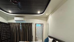 Een hotelkamer met een bed, een plafondventilator, een airconditioningapparaat, een donkere houten garderobe en een deur met een ruit.