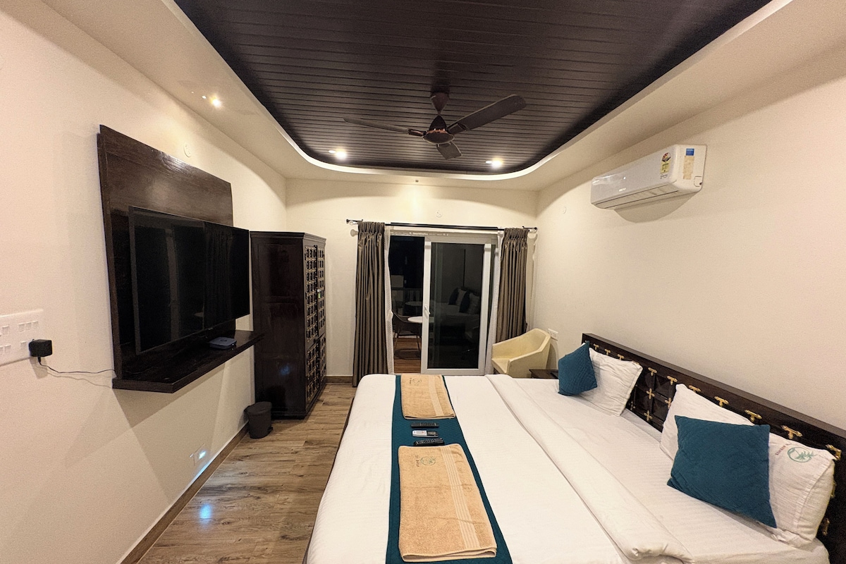 A hotel room with a bed, a television, a ceiling fan, and a sliding door leading to a balcony.