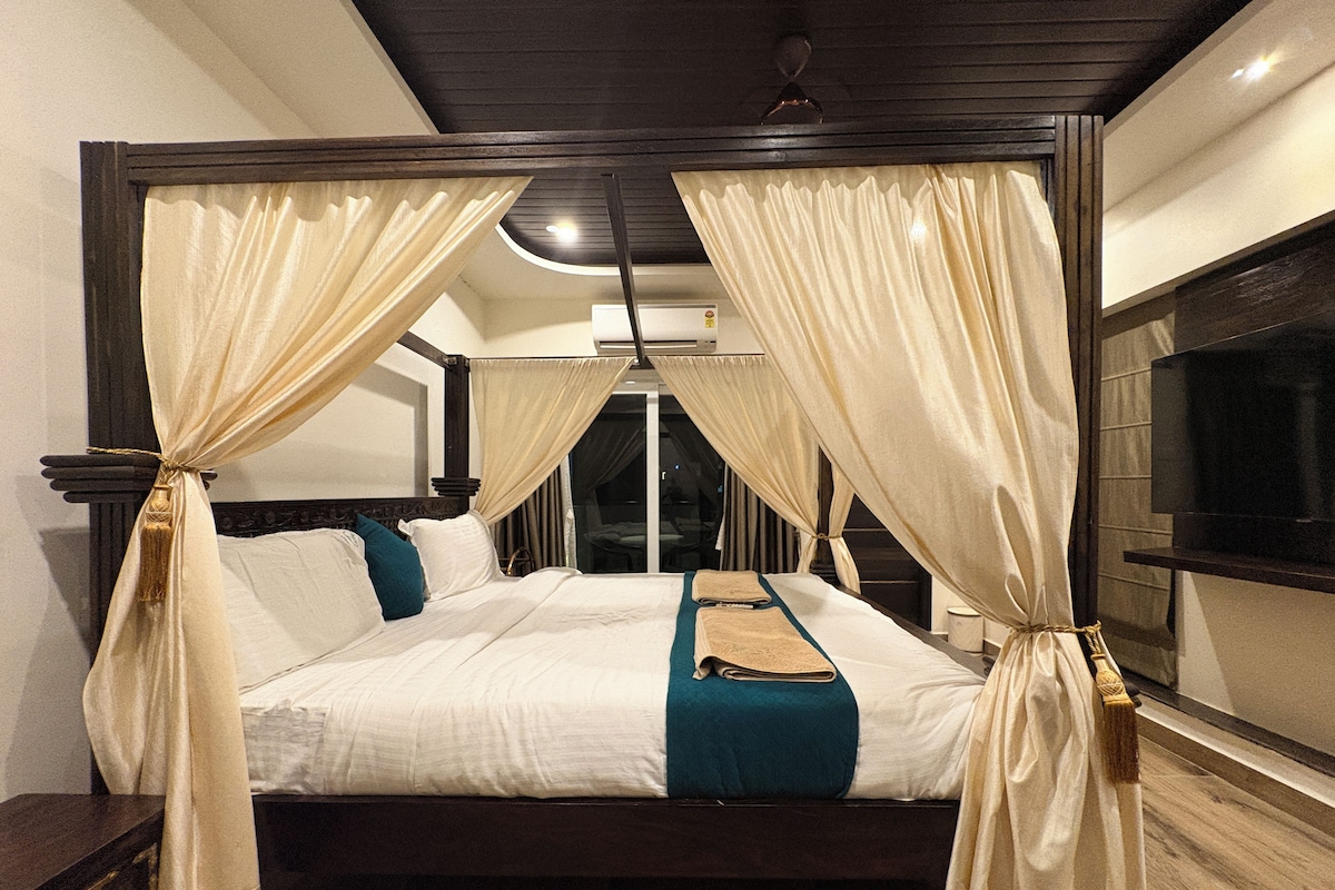 A four-poster bed with curtains, a flat-screen TV, and a wooden floor.