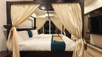 A four-poster bed with curtains, a flat-screen TV, and a wooden floor.