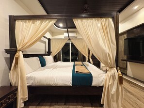 A four-poster bed with curtains, a flat-screen TV, and a wooden floor. - 5th Avenue (Visakhapatnam)