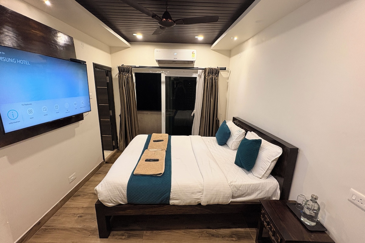A hotel room with a bed, a TV mounted on the wall, a ceiling fan, and an air conditioning unit.