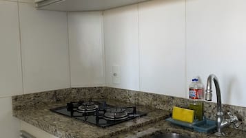 Uma cozinha com armários brancos, bancada de granito, fogão a gás, pia e dispensador de sabão.