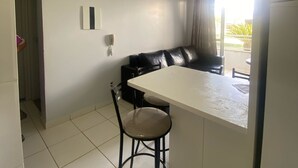A modern kitchen with a white countertop, a black chair, and a black leather sofa. - 1 bedroom apartment in Lagoa Quente flat service (Caldas novas)