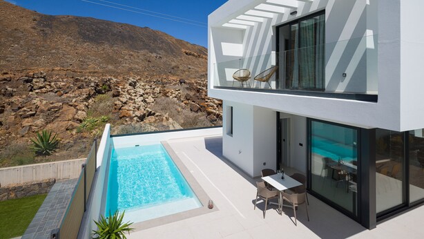 Ein modernes, zweistöckiges Gebäude mit Swimmingpool, Außenbereich und Blick auf felsiges Gelände.