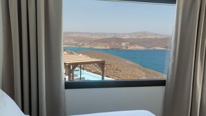 Quarto de hotel com cama, janela com cortinas e vista para a praia e o mar.