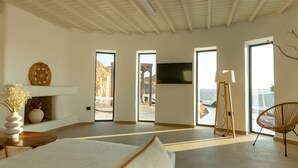 Quarto amplo com uma cama grande, TV fixada na parede e vista para o exterior pelas janelas.
