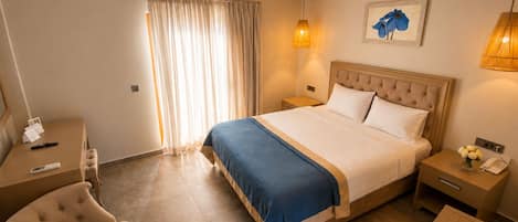Une chambre d’hôtel avec un lit, des tables de chevet, une chaise, un bureau, une lampe et un tableau au mur.