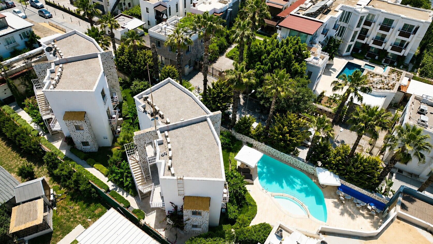 Vista aérea de una zona residencial con edificios modernos, una piscina y palmeras.