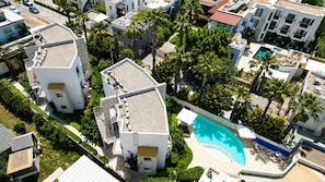 An aerial view of a residential area with modern buildings, a swimming pool, and palm trees. - Mercans Bodrum Beach Hotel (Bodrum)