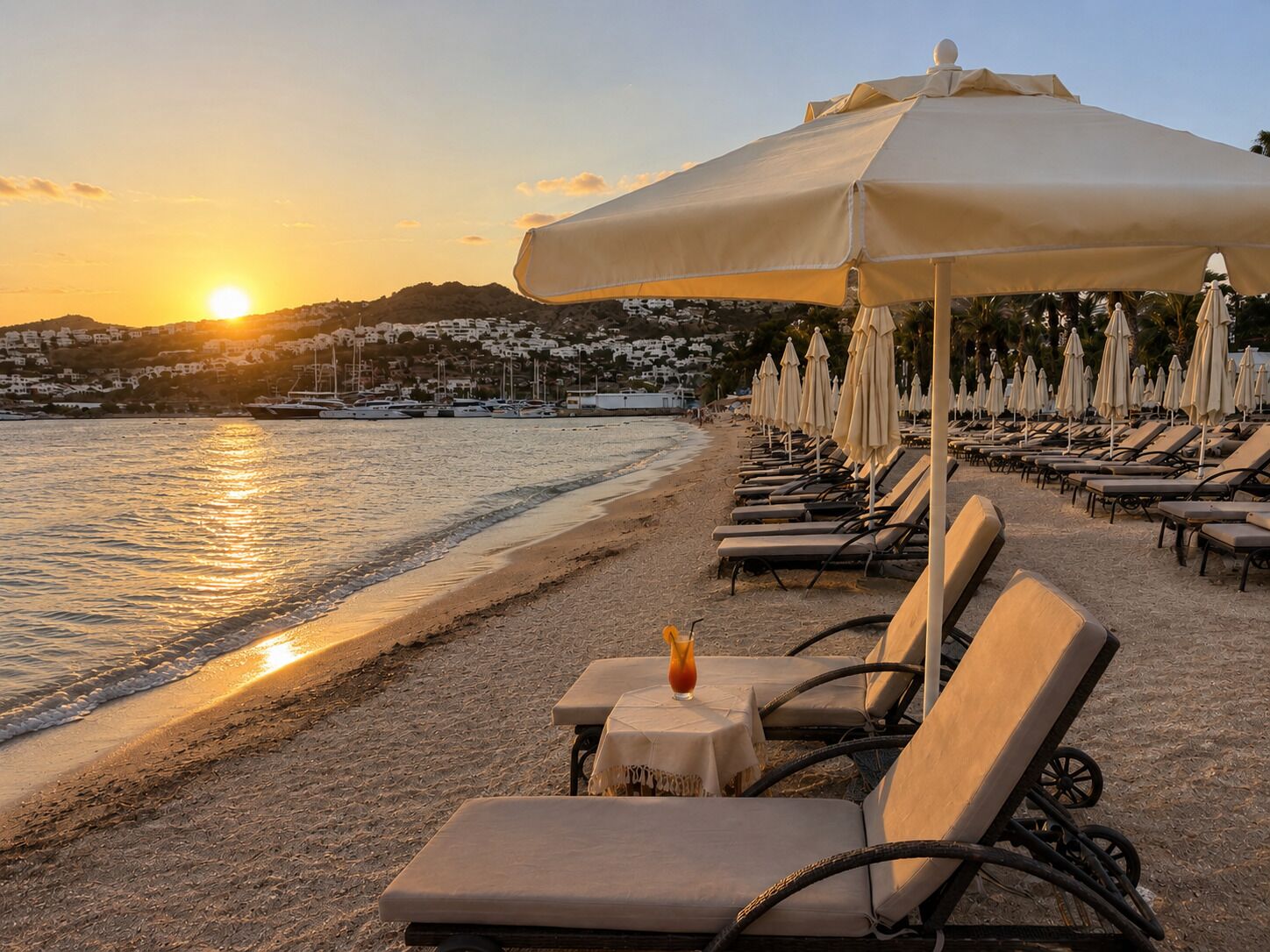 A beachside lounge area with sun loungers, umbrellas, and a table with a drink.
