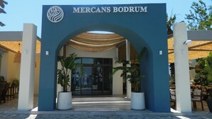 De ingang van Mercans Bodrum, met een blauwe boog, een logo, plantenbakken en een betegeld pad.