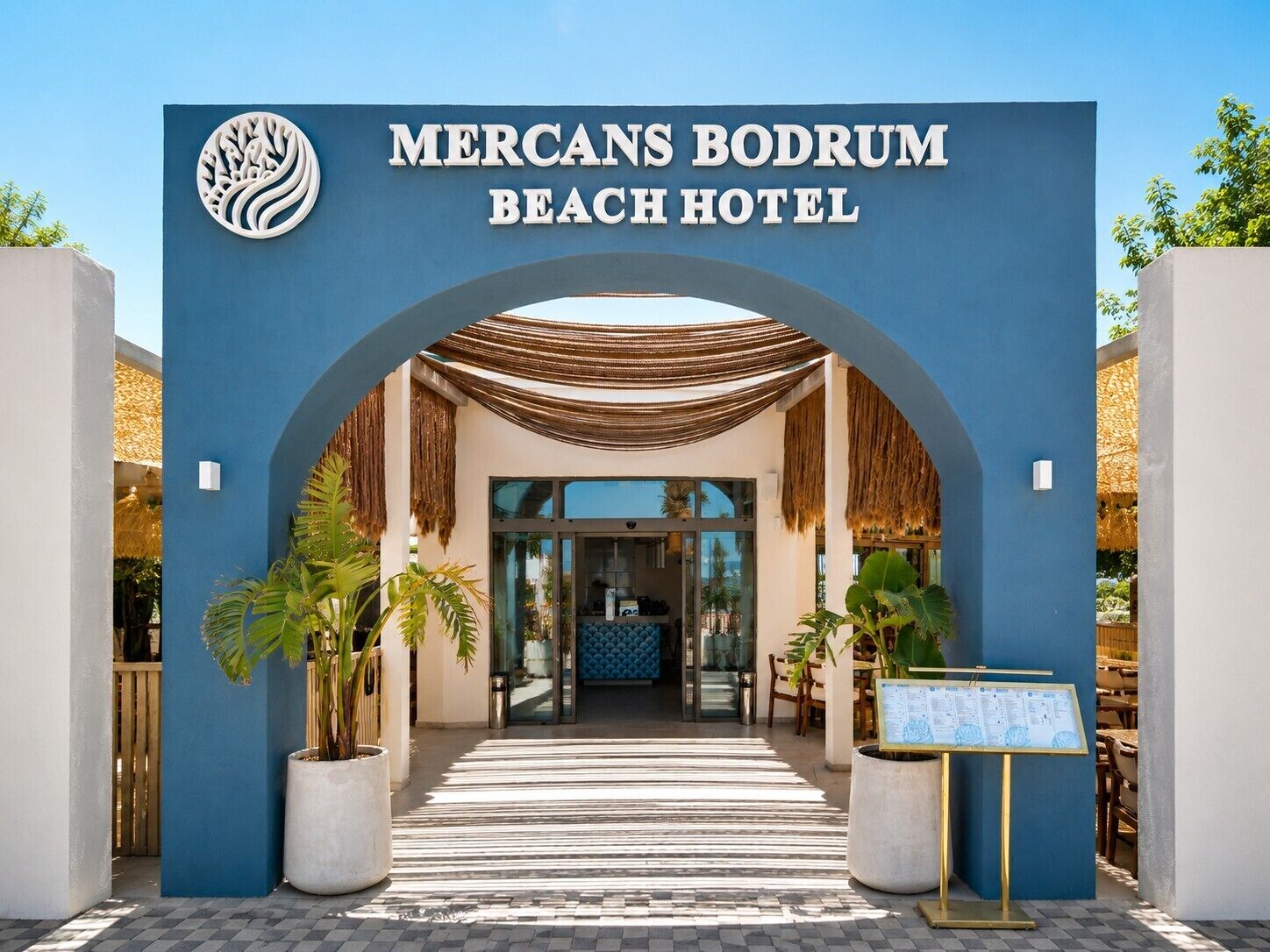 The entrance to Mercans Bodrum Beach Hotel with a blue facade, an archway, and a reception area visible inside.
