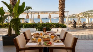 Een ontbijttafel met uitzicht op een strand met parasols en boten.