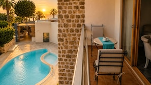 A poolside area with a stone wall, a table with a chair, and a view of the sunset. - Mercans Bodrum Beach Hotel (Bodrum)
