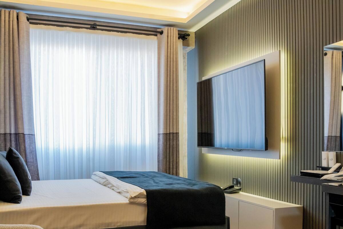 Et moderne hotelværelse med en seng, et tv ophængt på væggen, et lille bord og to stole.