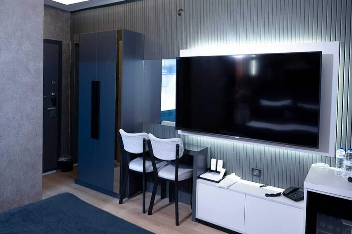 Et moderne hotelværelse med en stor seng, et fladskærms-tv, et skrivebord med en computer og et opholdsområde med stole.
