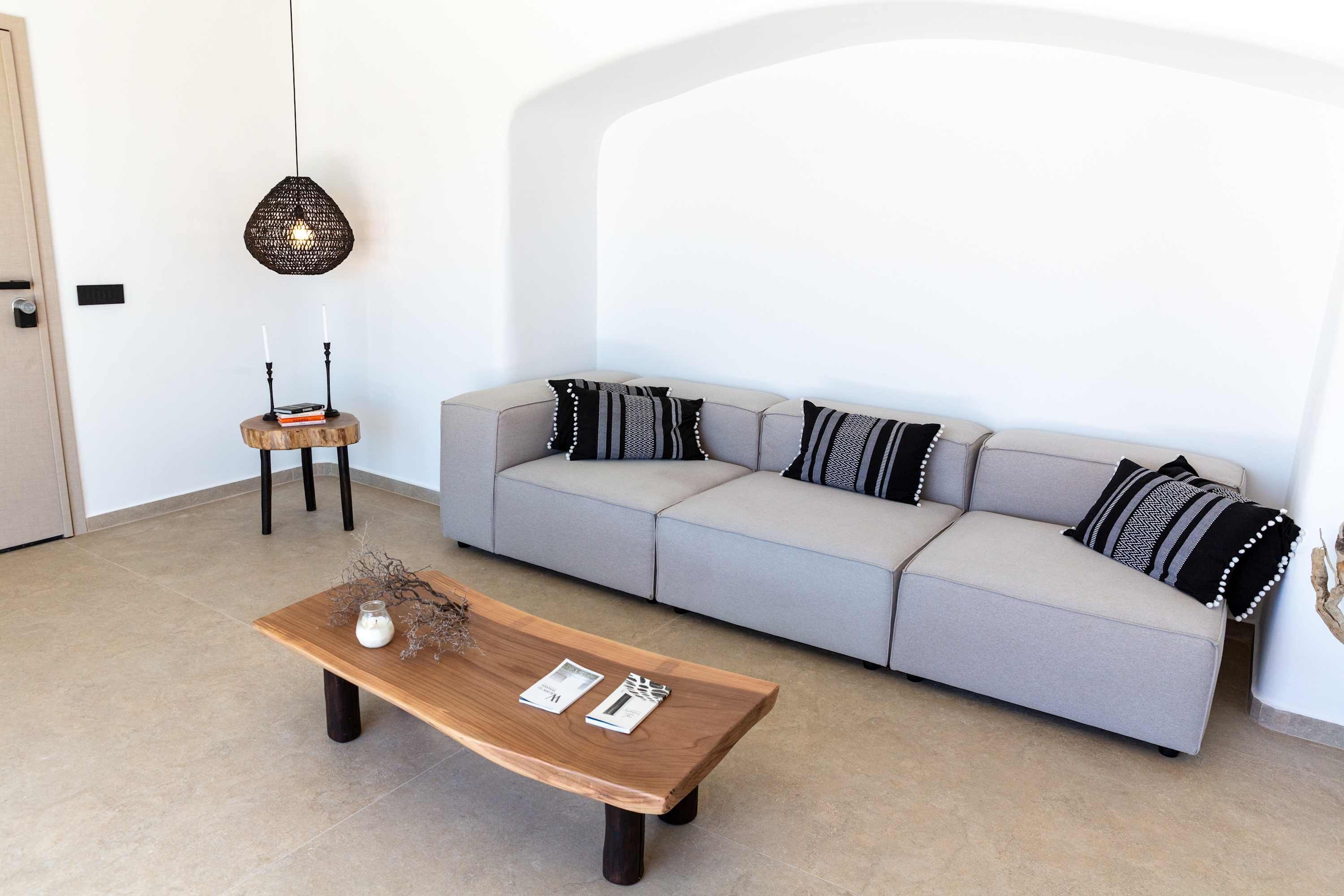 Ein modernes Wohnzimmer mit grauem Sofa, einem Holztisch und einer Pendelleuchte.