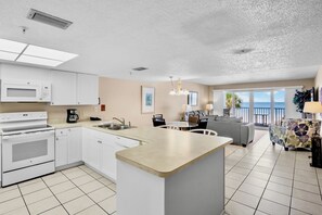 Cocina moderna con armarios blancos, una isla central y un comedor con vista al océano.